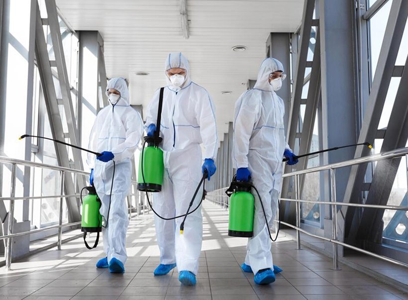 Three technicians in protective coveralls walking with spray equipment